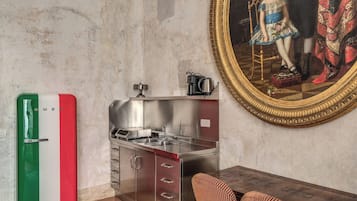 A compact kitchen with a sink, stove, and cabinets, a small dining table with chairs, and a framed painting on the wall.
