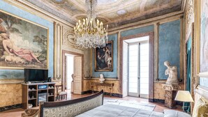 A luxurious bedroom with a large bed, a chandelier, and classical artwork. - Palazzo Doria Suites (Naples)