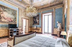 A luxurious bedroom with a large bed, a chandelier, and classical artwork.