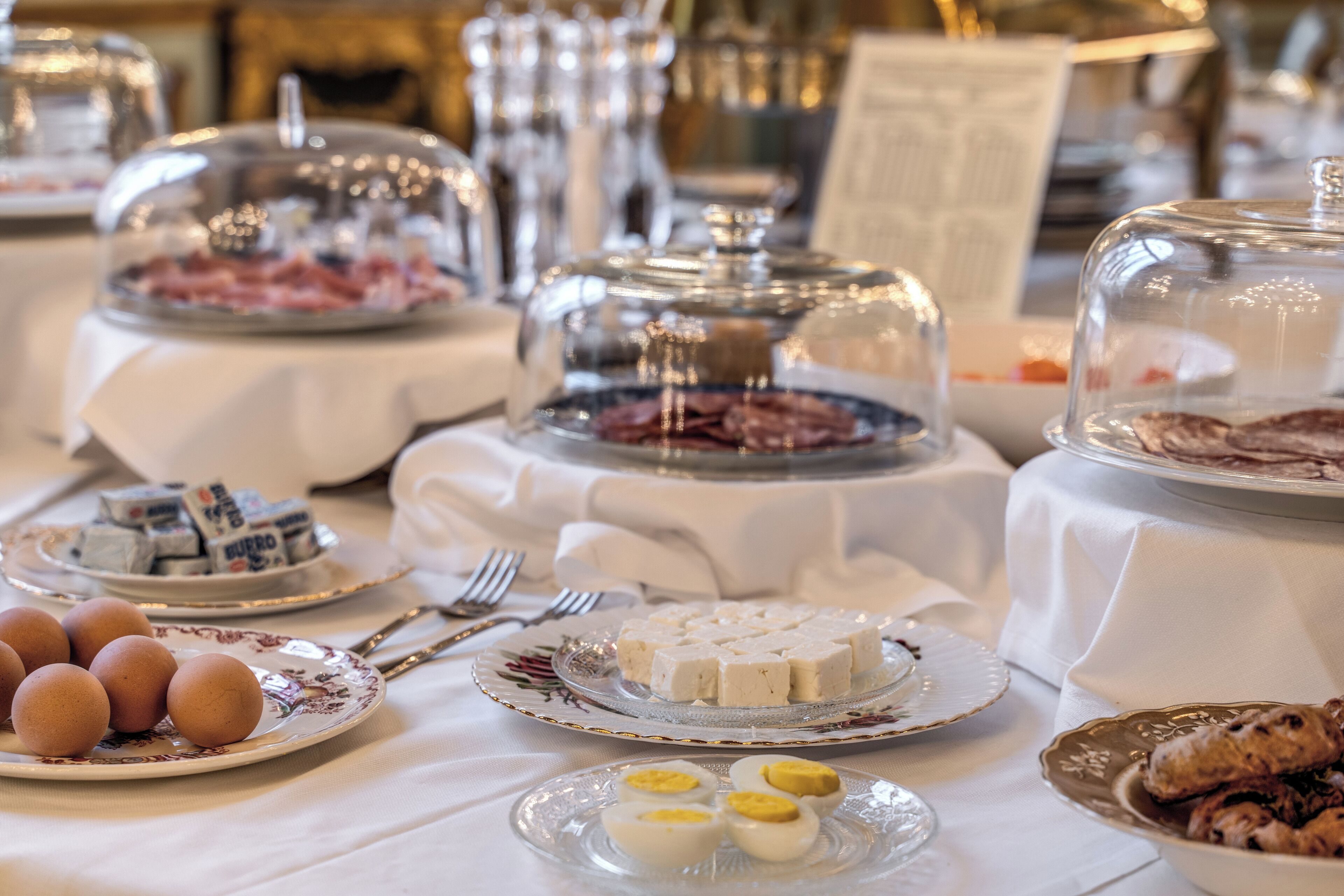 A buffet table with various food items, including eggs, cheese, and meat, covered with glass domes.