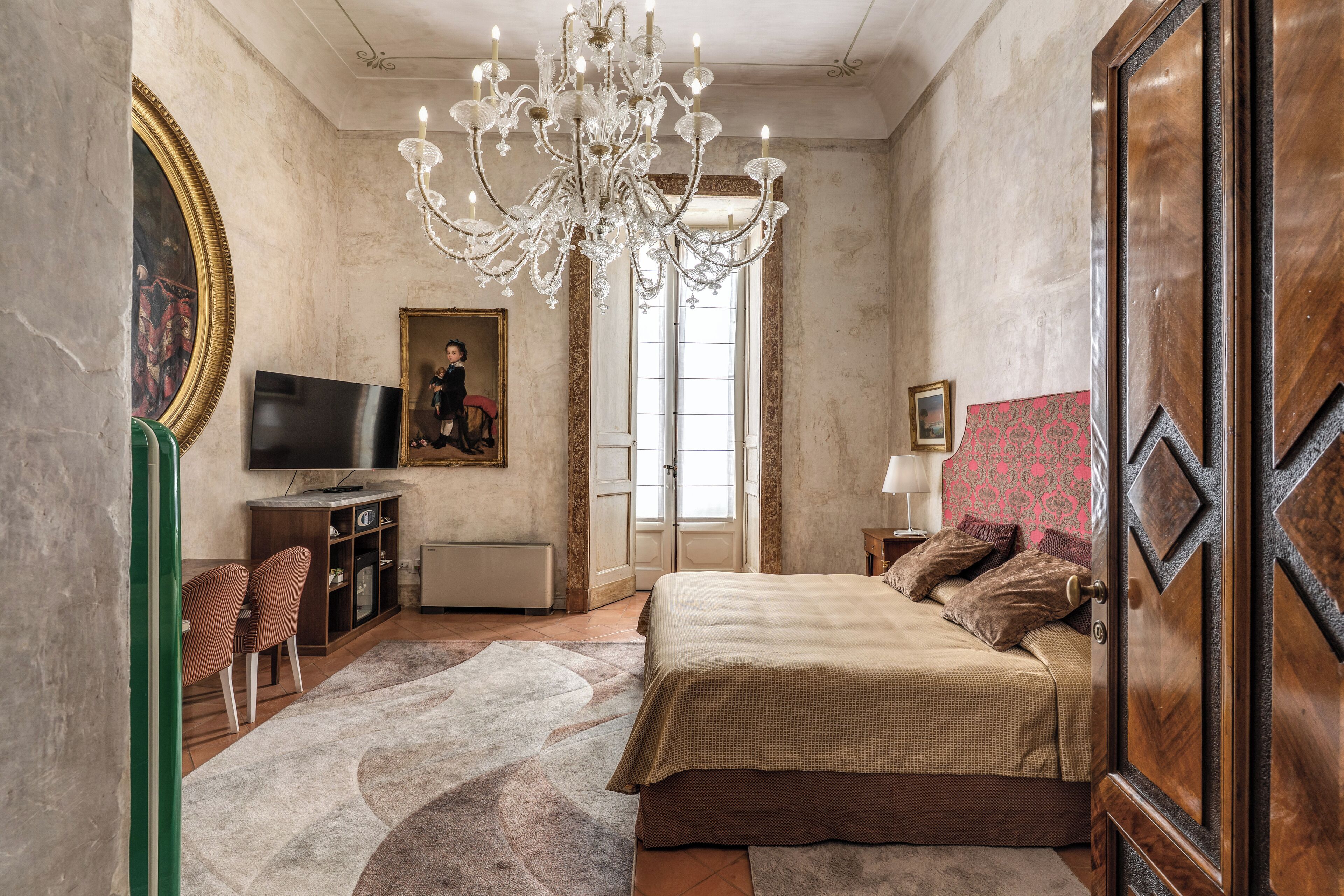 Un dormitorio con cama, televisor, candelabro y un cuadro en la pared.