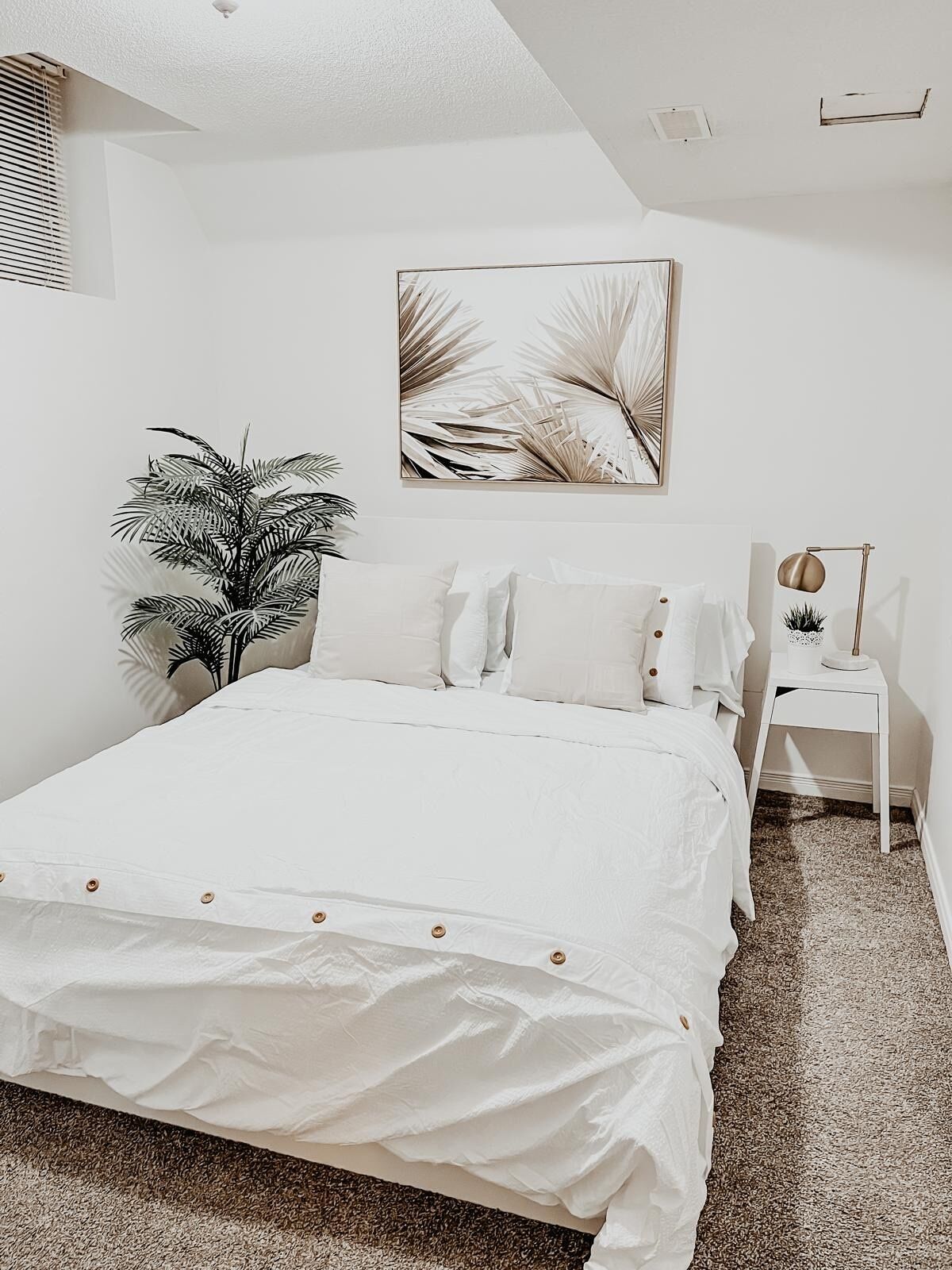 A bedroom with a large bed, a nightstand, a lamp, and a potted plant.