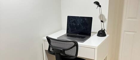 A white desk with a laptop and a desk lamp in a corner room with tiled flooring.