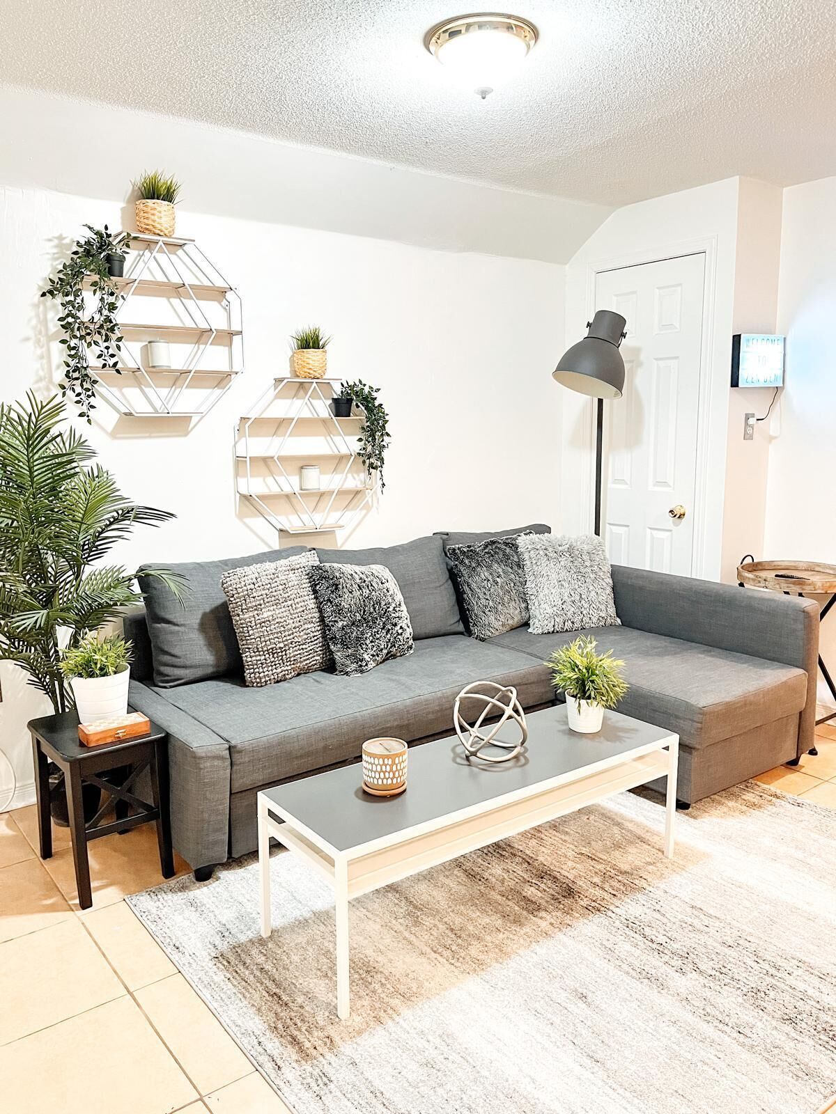 Una sala de estar moderna con un sofá gris, una mesa de centro blanca y plantas decorativas.