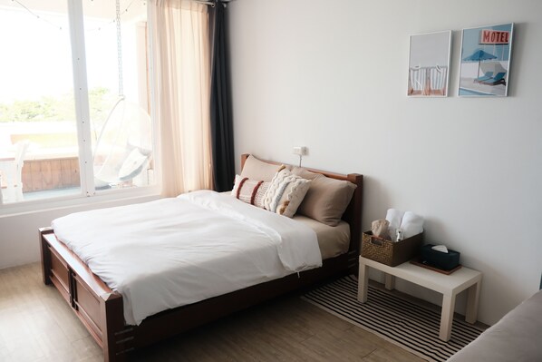 A neatly made bed with a white comforter and pillows, a bedside table with a tissue box and a basket, and a wall with two framed pictures. - Solchill Inn (Hengchun)