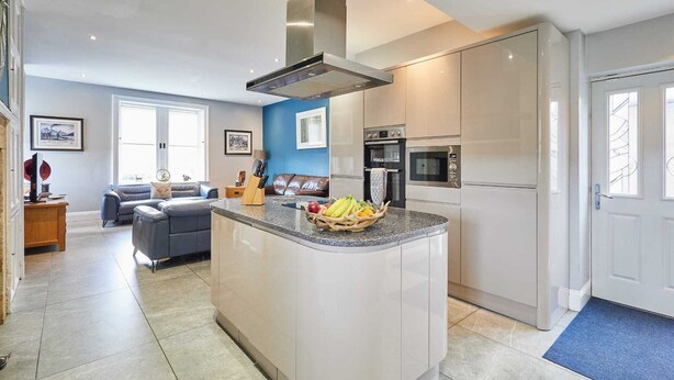 Cocina moderna con una isla central, electrodomésticos integrados y una zona de estar con sofá y mesa de centro.