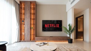 A modern living room with a large flat-screen TV displaying 'NETFLIX', a wooden accent wall, a round coffee table, and a potted plant. - KeyRock - Palm View Luxury Stay in GB (Dubai)