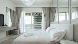 A modern hotel room with a large bed, a flat-screen TV, a desk, and a view of the city through large windows. - KeyRock - Palm View Luxury Stay in GB (Dubai)