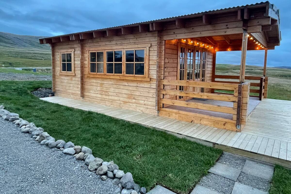 A wooden cabin with a porch, large windows, and a stone pathway leading to it.