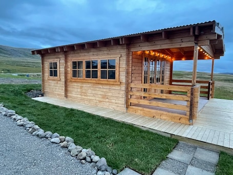 A wooden cabin with a porch, large windows, and a stone pathway leading to it.