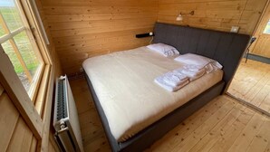 A wooden-paneled room with a bed, a window, and a radiator. - Hvammstangi Rhino Rock Cottages (Hvammstangi)