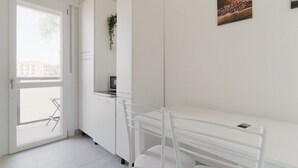A modern kitchen with white cabinetry, a dining area with a white table and chairs, and a window with a view of buildings outside. - GuestHost - Comfortable 40 sqm apartment, accommodating up to two people, located on the fourth floor of a building with an elevator (NOT wheelchair accessible).The property is located just steps from Piazzale Tripoli, in a residential area with all amen (Milan)