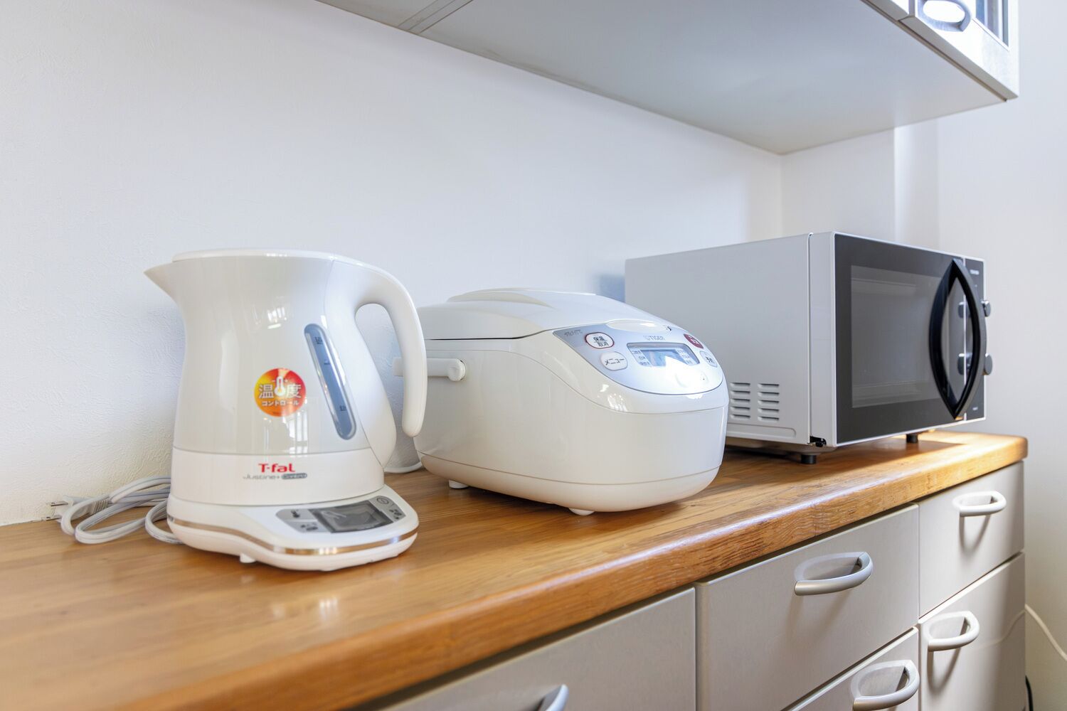 A kitchen counter with a kettle, rice cooker, and microwave.