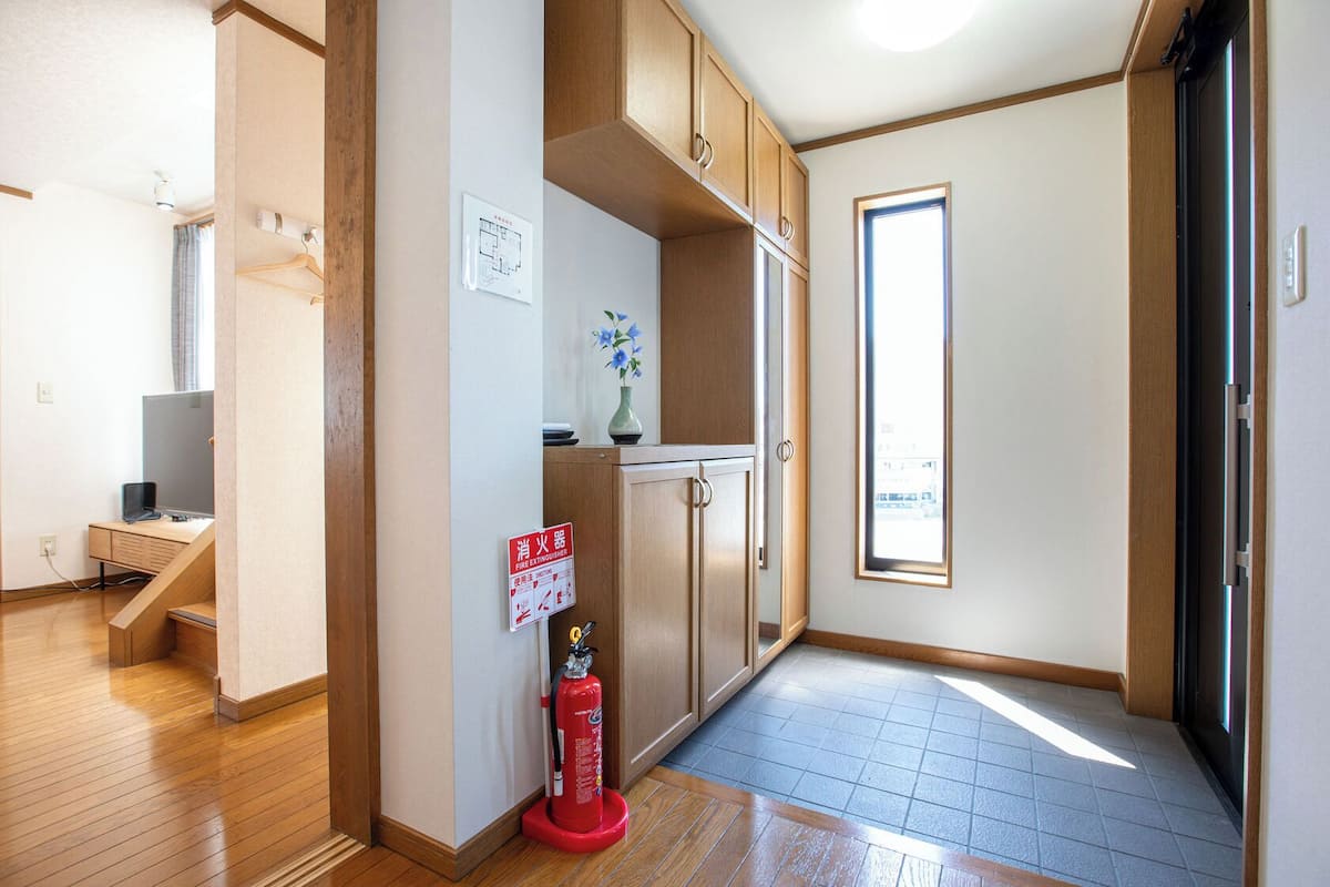 A hallway with wooden cabinets, a fire extinguisher, a small desk with a computer, and a window with a view of buildings.