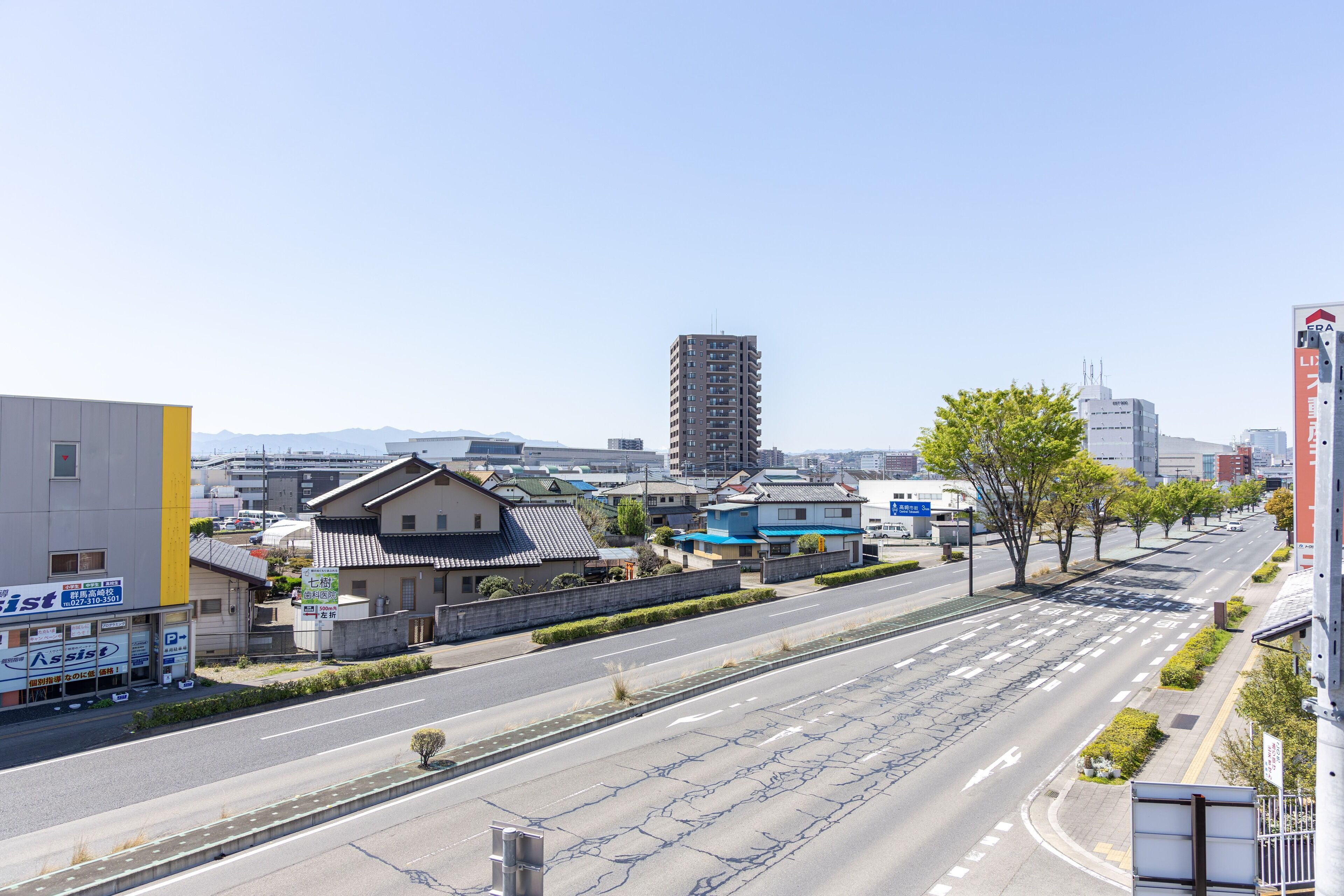 A wide, multi-lane road with buildings on both sides, including a tall residential building and a commercial building with signage.