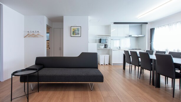 En moderne stue med sofa og spisebord med stole. Der er et tekøkken med skabe og en mikrobølgeovn.