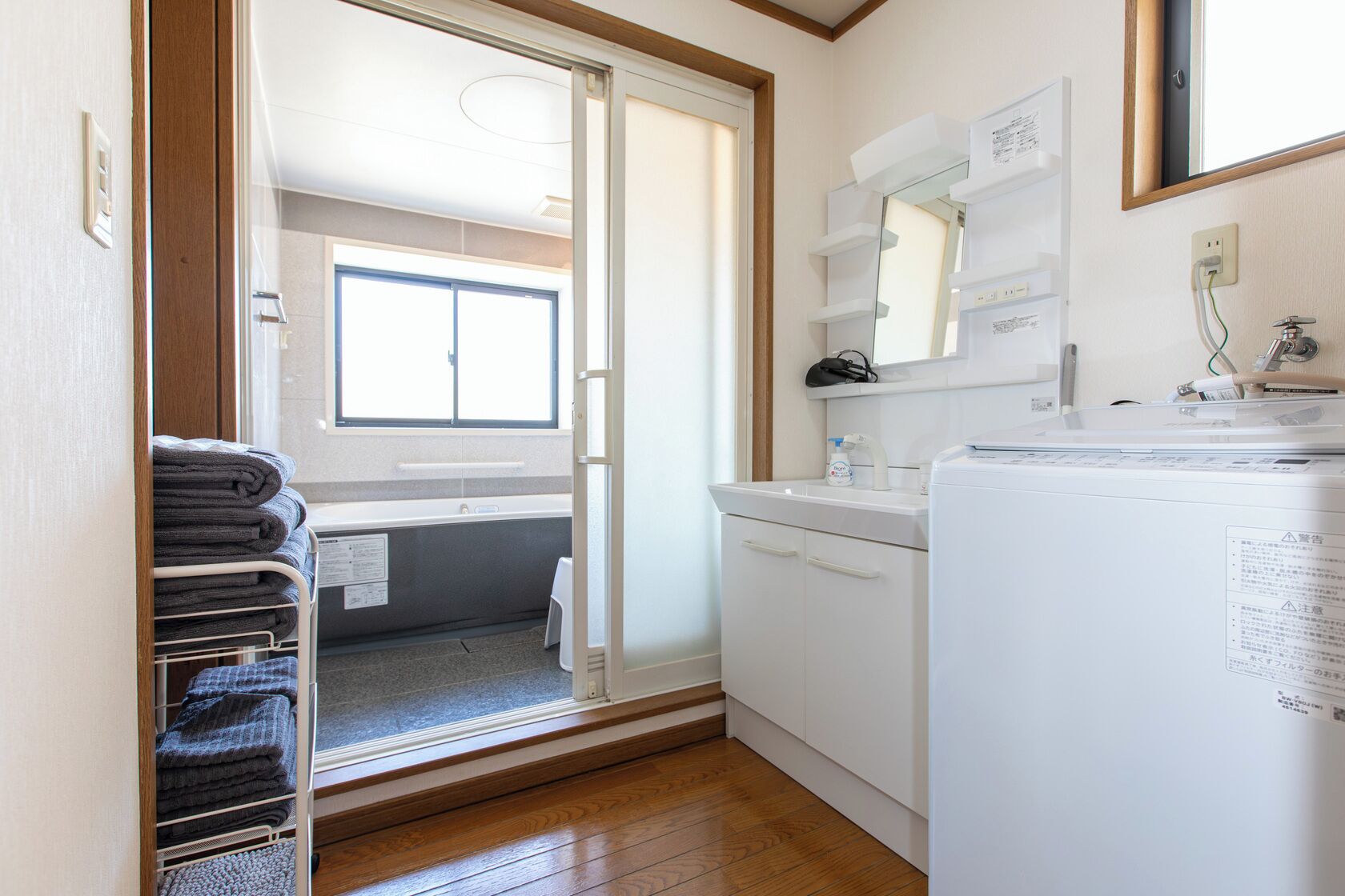 Uma casa de banho compacta com chuveiro, lavatório e sanita. Há uma pilha de toalhas num suporte e um espelho acima do lavatório.