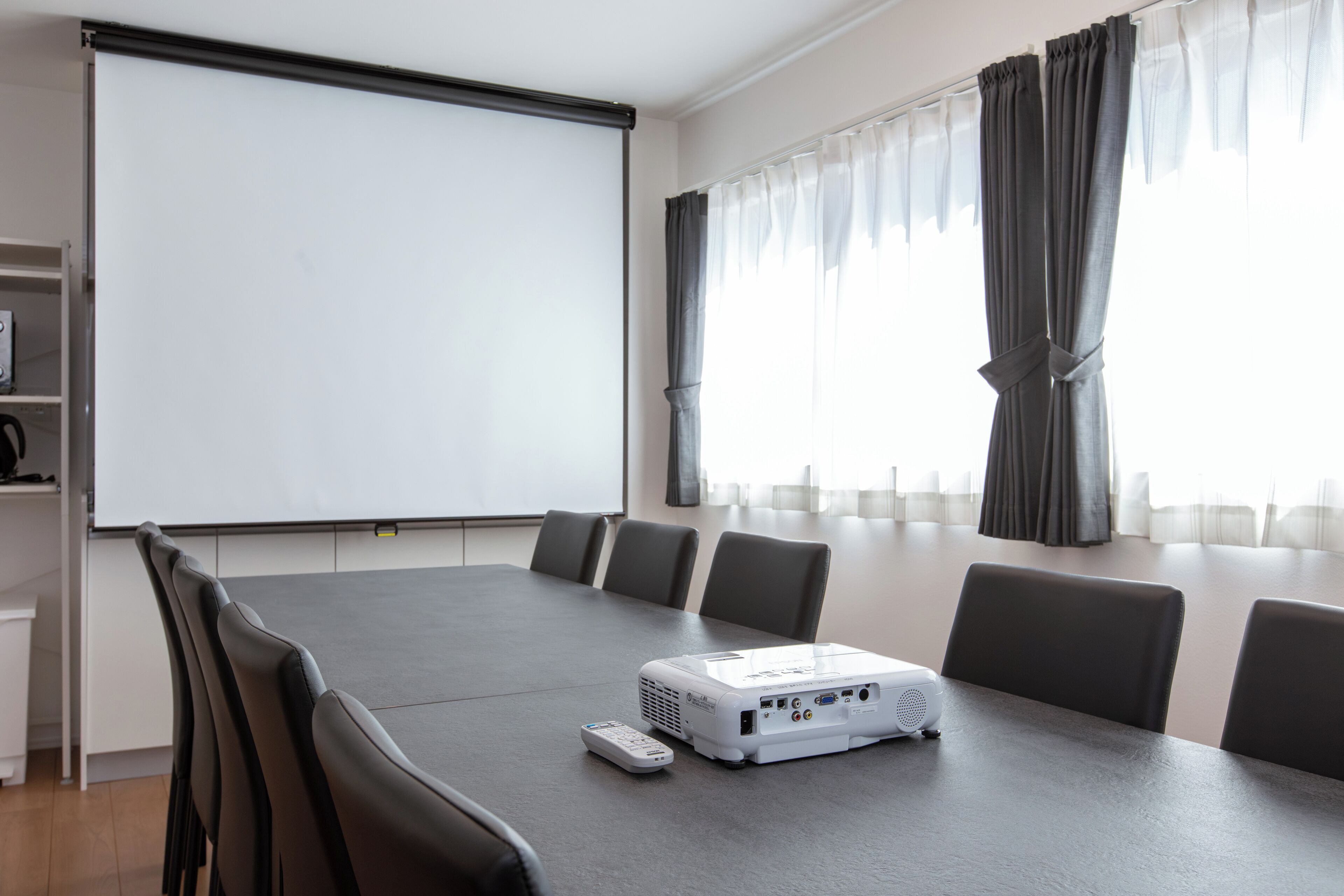 Una sala de conferencias con un proyector, una pizarra y una gran mesa con sillas.