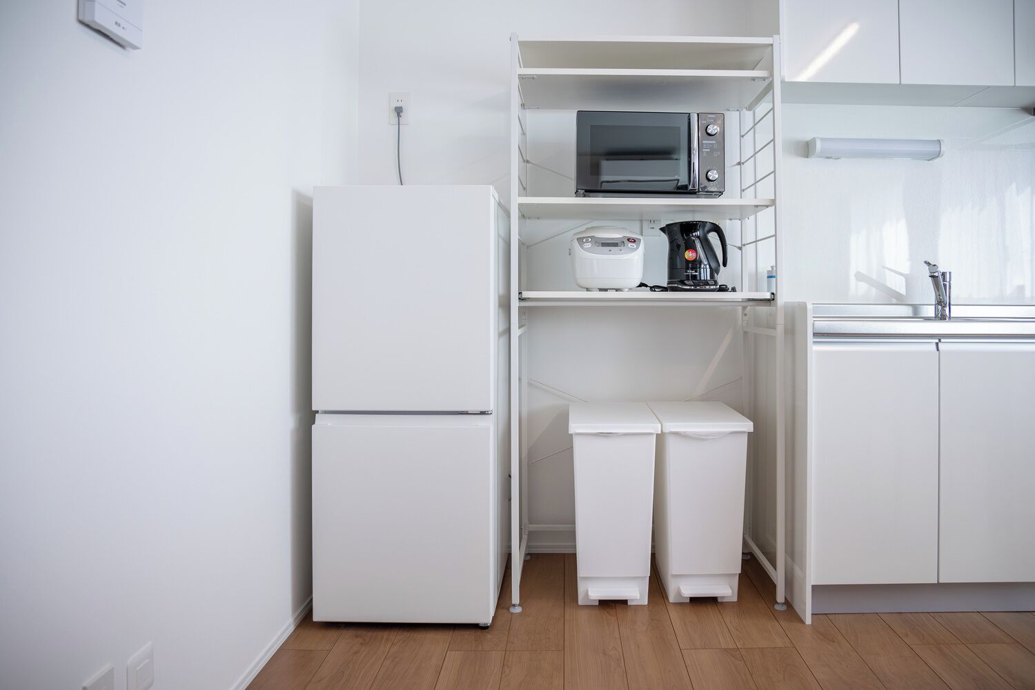 A compact kitchen with a white refrigerator, a microwave, and a kettle on the countertop.