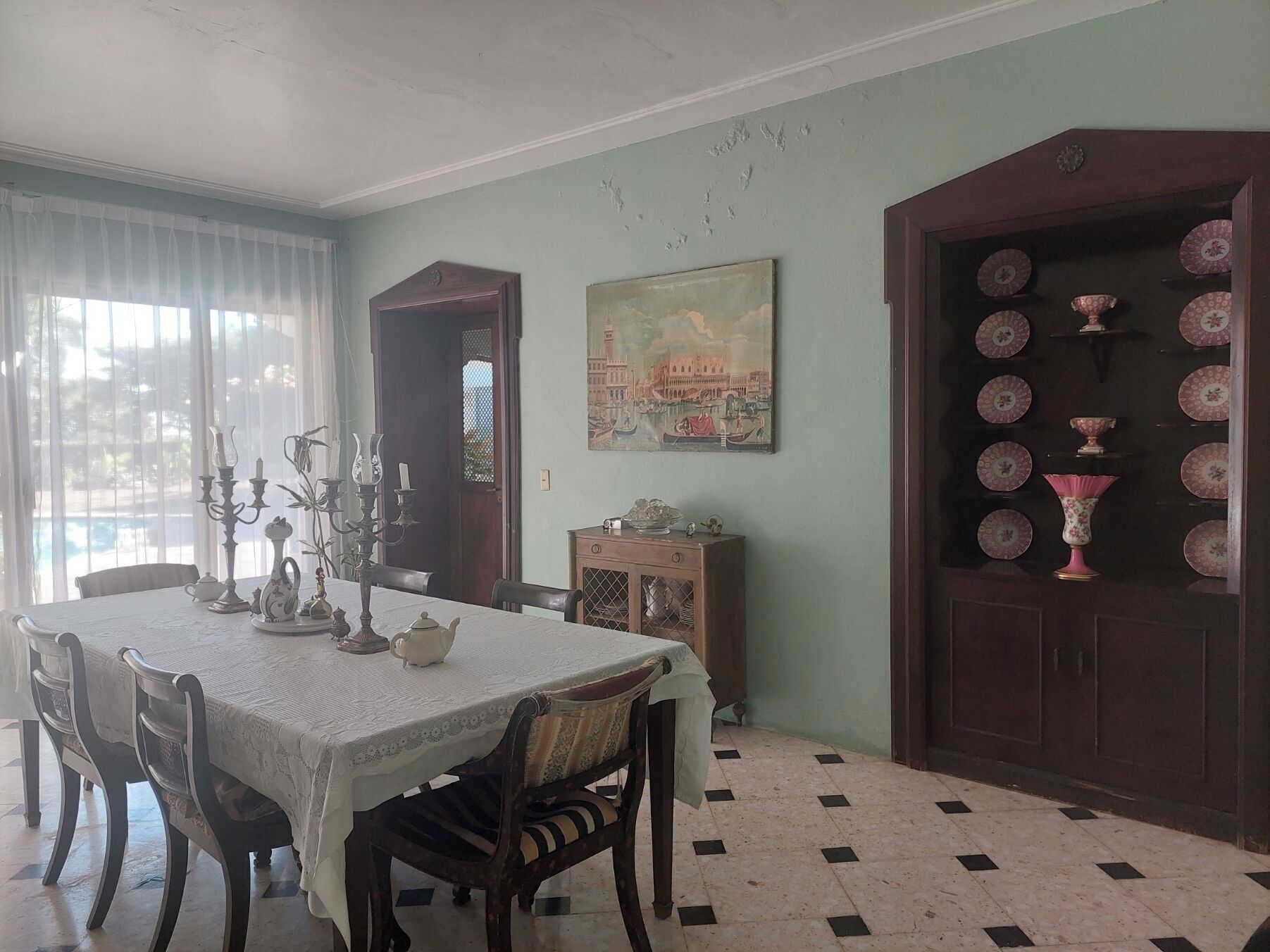 A dining room with a table set for four, a painting on the wall, and a cabinet with plates.