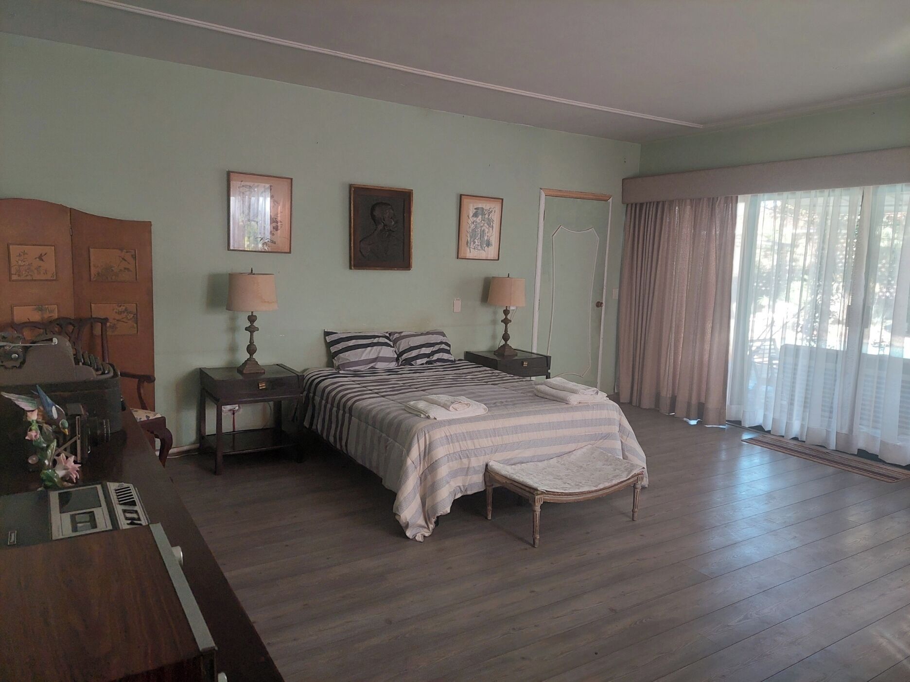 Une chambre à coucher comprenant un lit, deux tables de chevet, une commode, une coiffeuse et une fenêtre avec des rideaux.