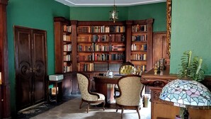 A library with wooden bookshelves, a desk, two chairs, and a stained glass lamp. - Casa del Roble 1 Residence (Cuernavaca)