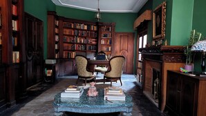 A library with bookshelves, a wooden desk, two chairs, a marble table, and a fireplace. - Casa del Roble 1 Residence (Cuernavaca)