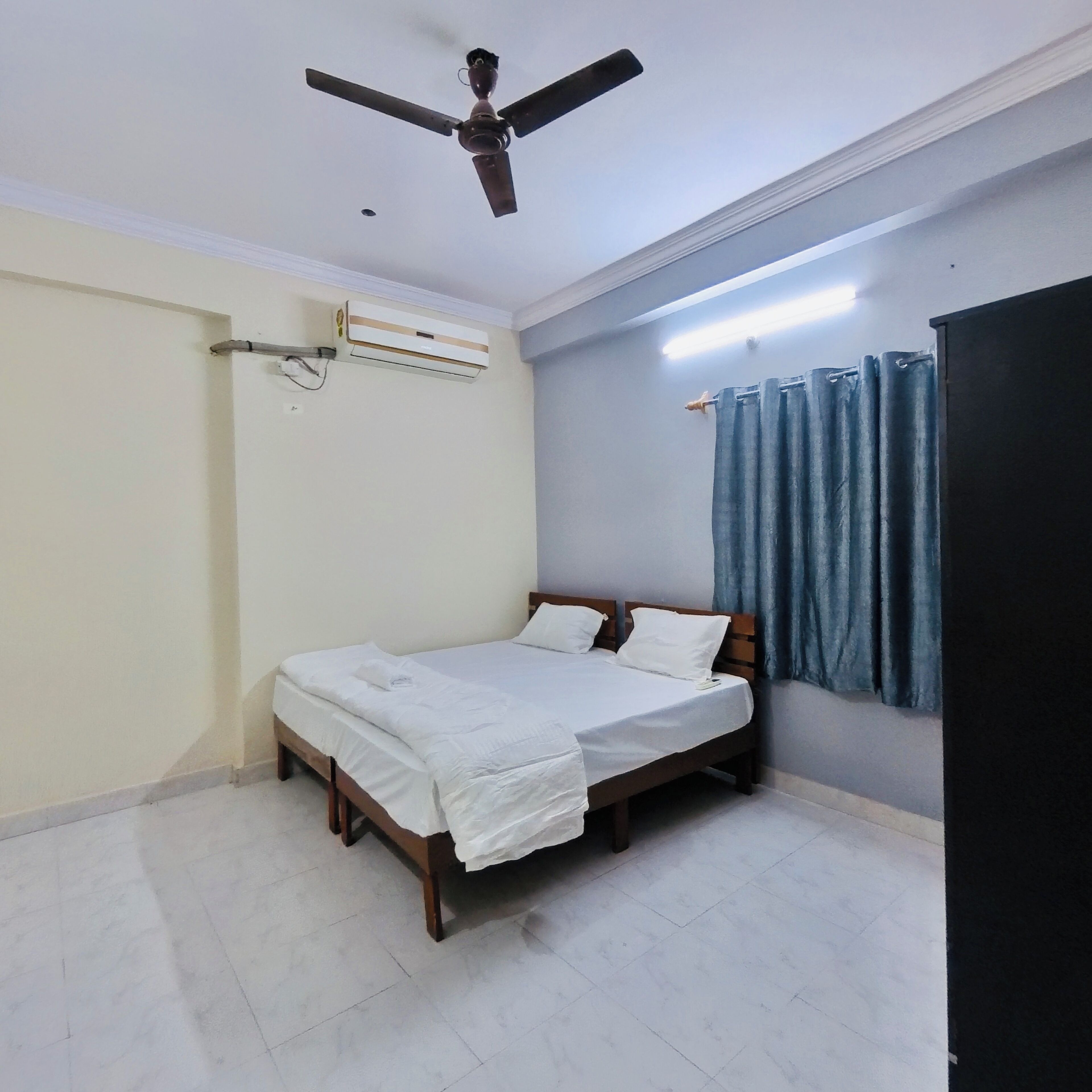 Une chambre à coucher comprenant un lit, un ventilateur de plafond, un appareil de climatisation, un rideau et une étagère fixée au mur.
