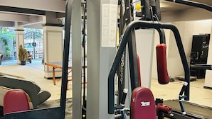 A gym with exercise equipment, a mirror, and a door leading to an outdoor area with plants and a gate.