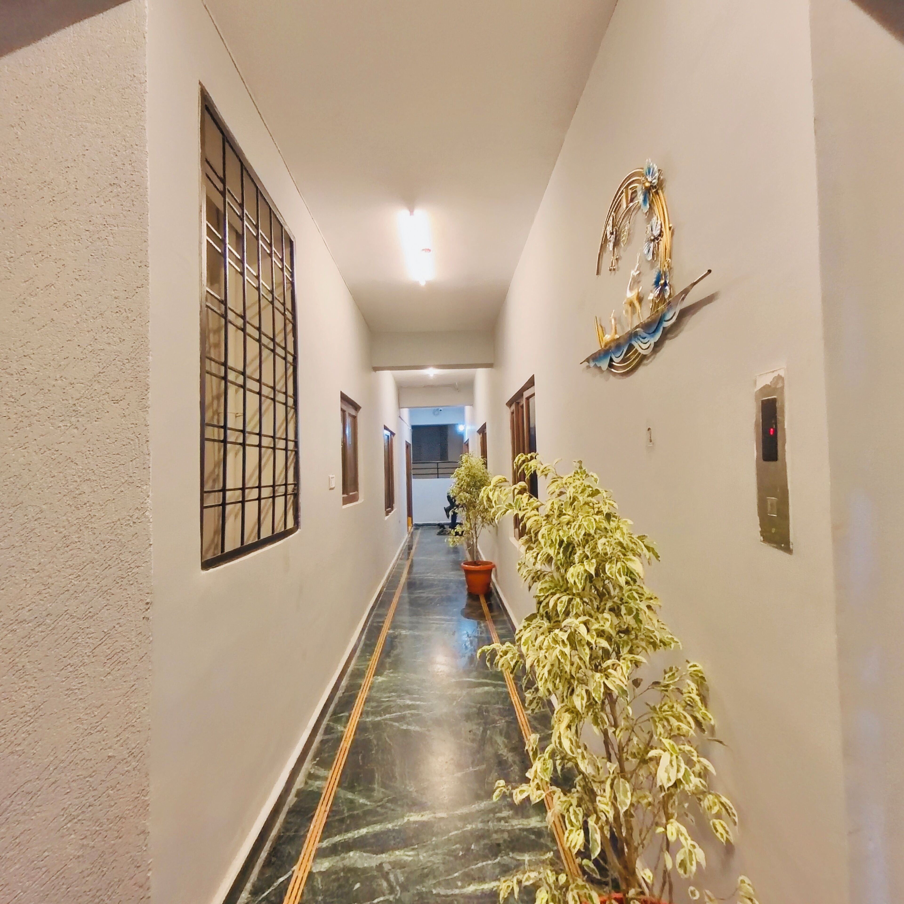 A corridor with a marble floor, a potted plant, and a decorative wall piece.