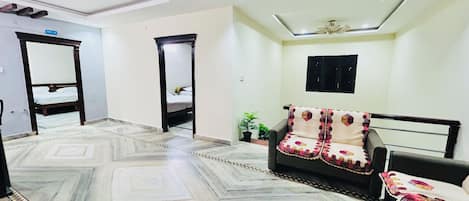 A spacious room with a patterned marble floor, a sofa with a decorative throw, a ceiling fan, and a bed in the background.