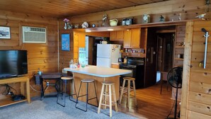 A wooden cabin interior with a kitchen area, bar stools, a refrigerator, a stove, and a television. - Fabulous 2-bedroom Otsego lake cottage in charming Gaylord (Gaylord)