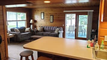 L’intérieur de la cabine est en bois et comprend un coin repas avec une table et des chaises, un ensemble de canapés et un coin cuisine avec un évier et des tabourets de bar.