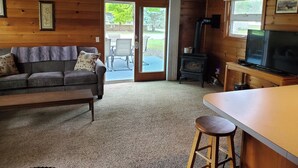 A cozy cabin interior with a sofa, a television, a wooden table, and a fireplace. - Fabulous 2-bedroom Otsego lake cottage in charming Gaylord (Gaylord)