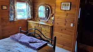 A wooden cabin bedroom with a bed, dresser, mirror, and window with curtains. - Fabulous 2-bedroom Otsego lake cottage in charming Gaylord (Gaylord)