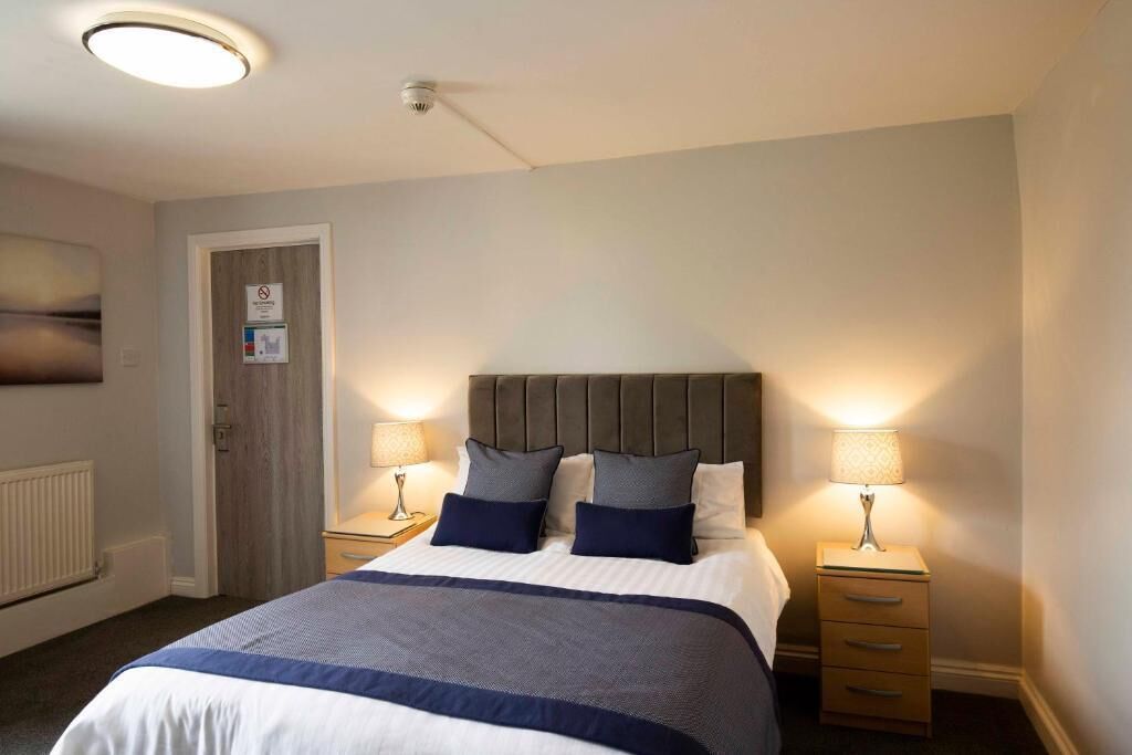 Et hotelværelse med en stor seng, to sengeborde med lamper, en dør med et skilt og en loftlampe.