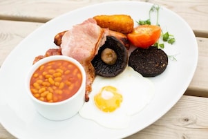 Um prato com diversos itens de café da manhã, incluindo ovos, feijão, bacon e uma fatia de tomate.