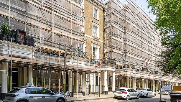 Un edificio de varios pisos con fachada en construcción, que incluye balcones y una entrada desde la calle.