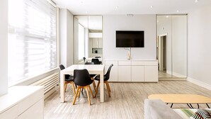 Un comedor moderno con una mesa blanca, sillas negras y un televisor de pantalla plana montado en la pared.