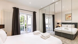 Habitación de hotel con una cama grande, balcón, pared con espejo y vista al exterior.