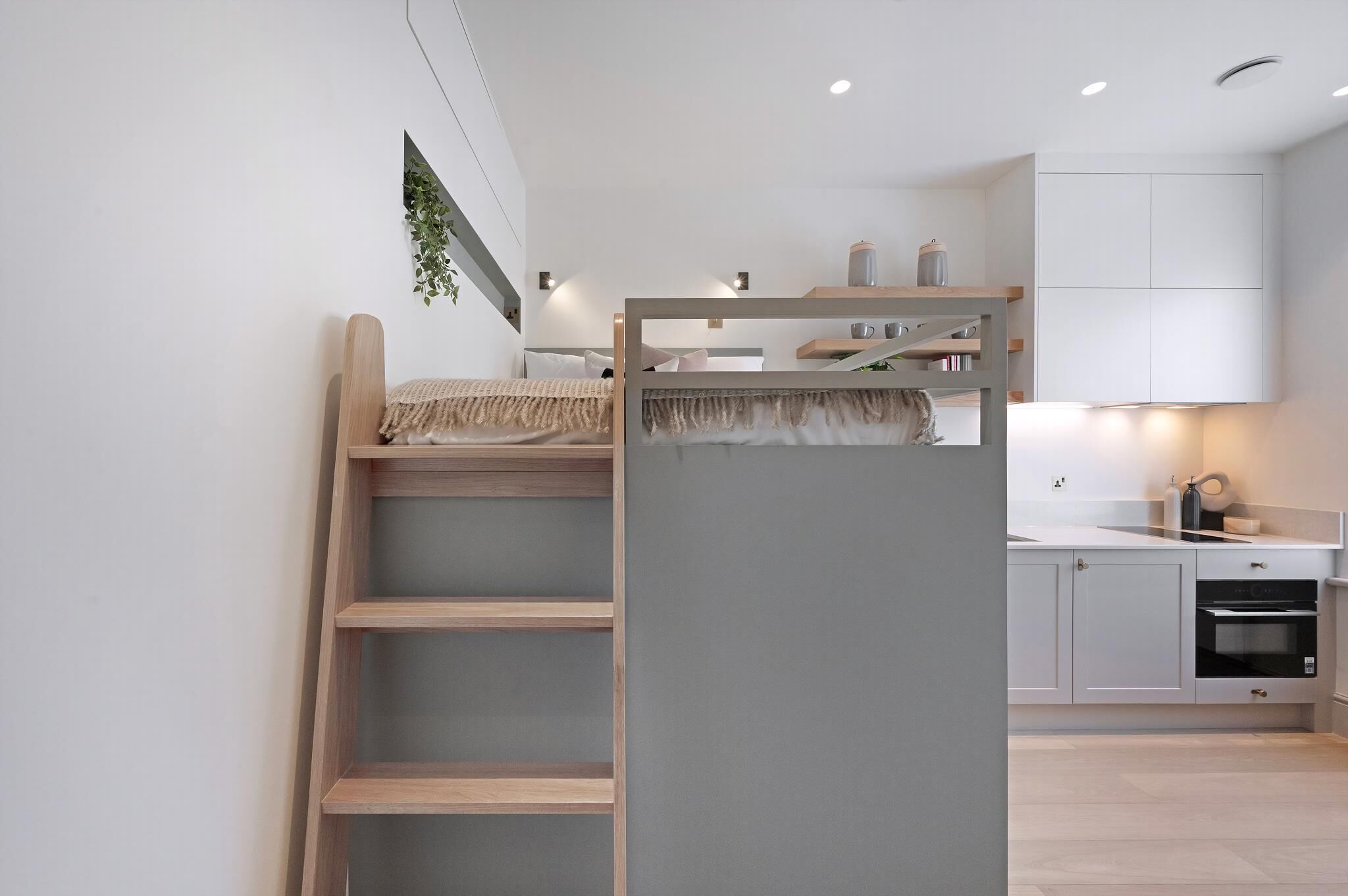 A modern, compact room with a bunk bed, a small kitchenette, and a wall-mounted shelf.