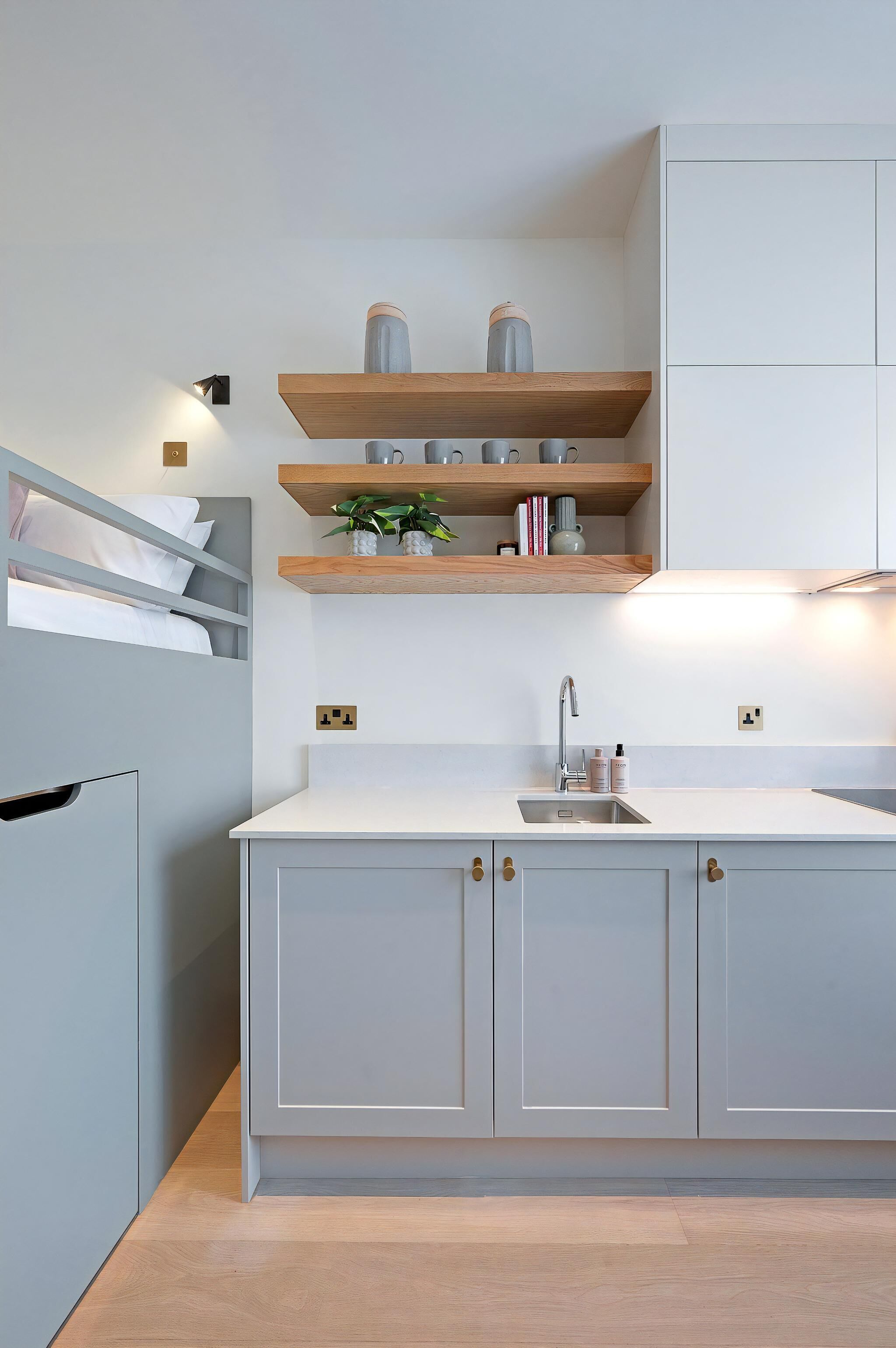 Eine moderne Küche mit grauen Schränken, Holzregalen und einem eingebauten Bett.