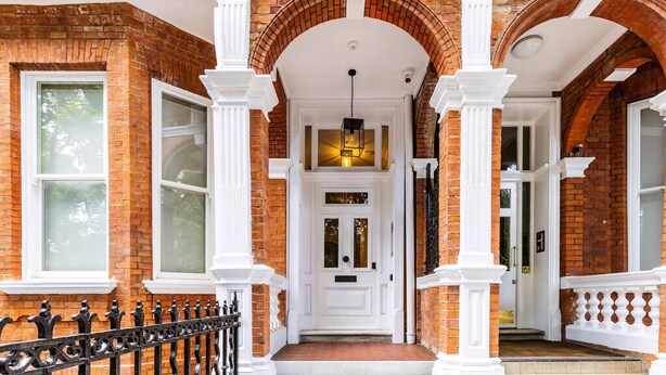 A brick building with a white door, white columns, and a black wrought iron fence. - The Mezzanine Studio at Bramham (London)