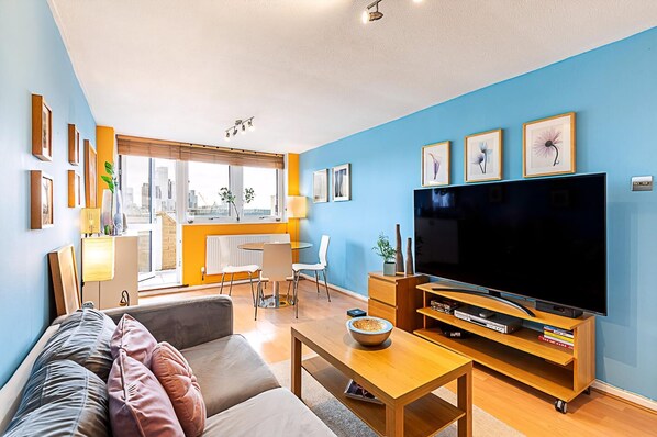 A modern living room with a large flat-screen TV, a sofa, a coffee table, and a dining area with a table and chairs.