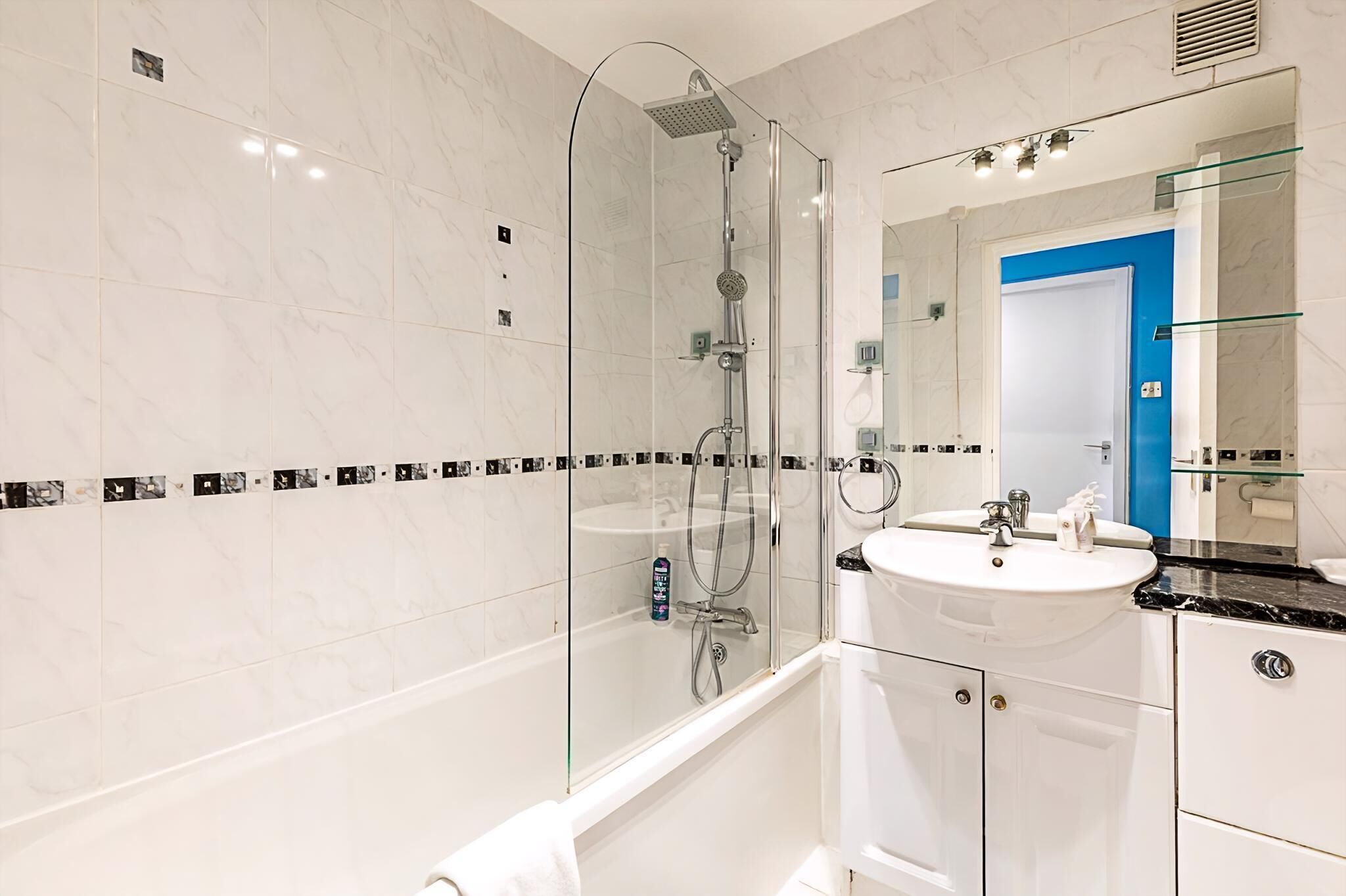 A modern bathroom with a glass-enclosed shower, a white sink, and a blue door.