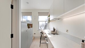 A modern kitchen with a central island, built-in appliances, and a window providing natural light. - The Lightwell Studio at Bramham Gardens (London)