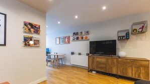 A modern living room with a wooden cabinet, a TV, and framed artwork on the wall. - Stylish Deptford Flat With Private Terrace (London)