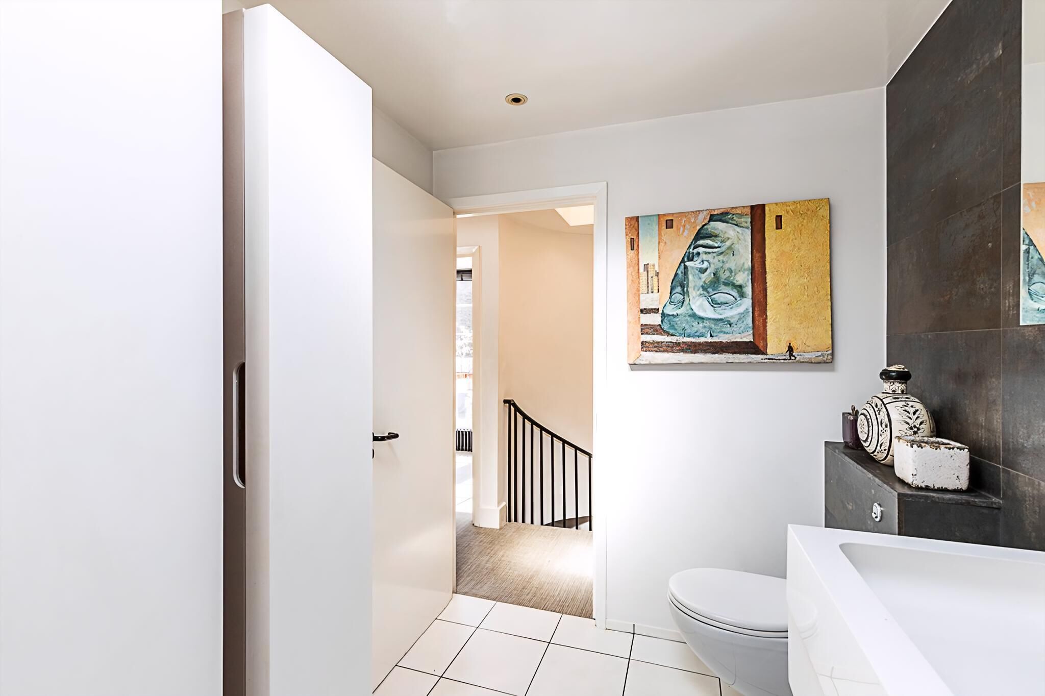 Ein modernes Badezimmer mit Toilette und Badewanne in Weiß, sowie einem großen abstrakten Gemälde an der Wand.