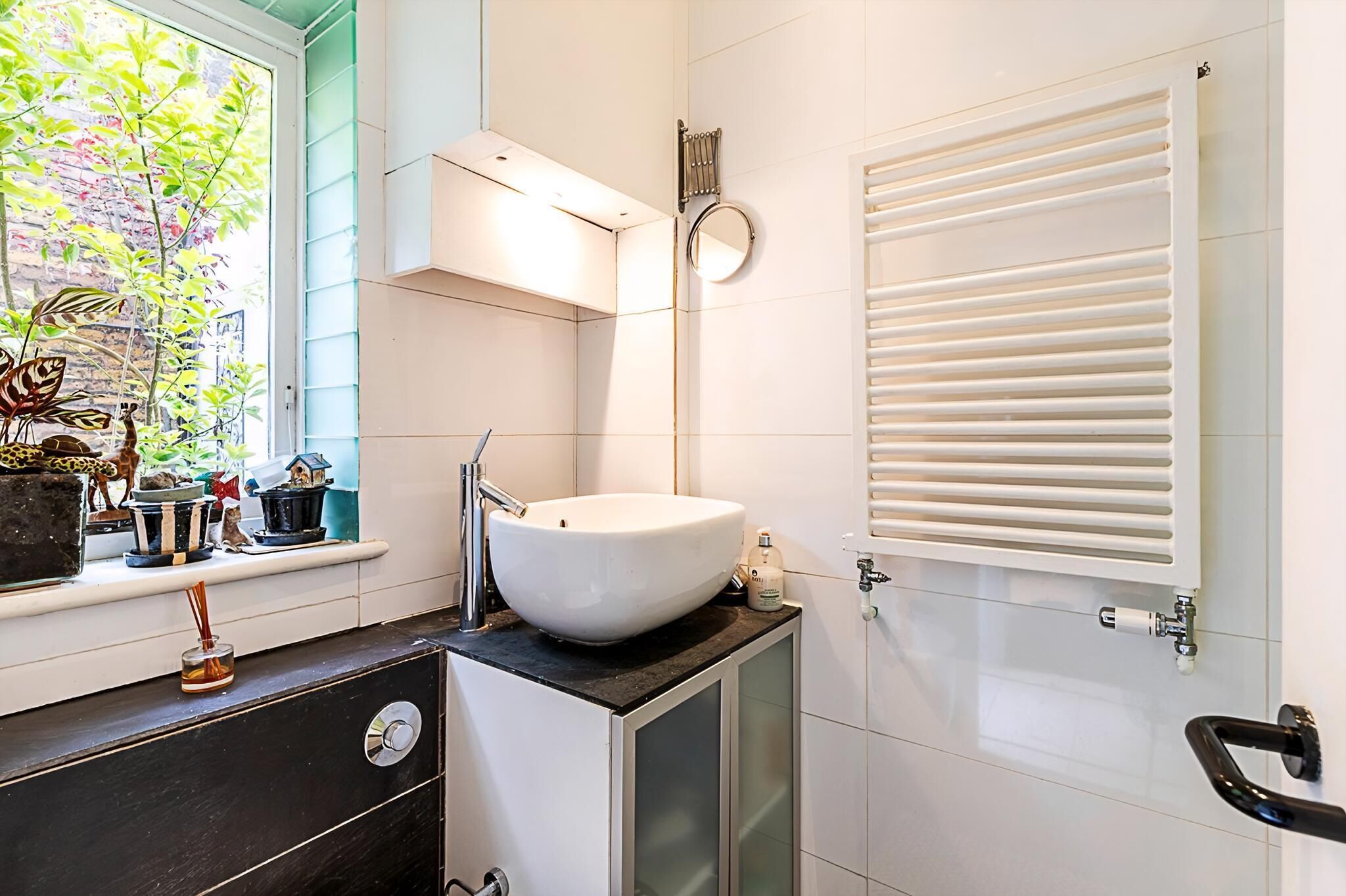 A modern bathroom with a white sink, a mirror, and a window with a view of greenery.