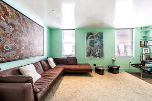 A modern living room with a brown sectional sofa, a large abstract painting, and a bookshelf. - Stylish Mews Home in Kensington (London)